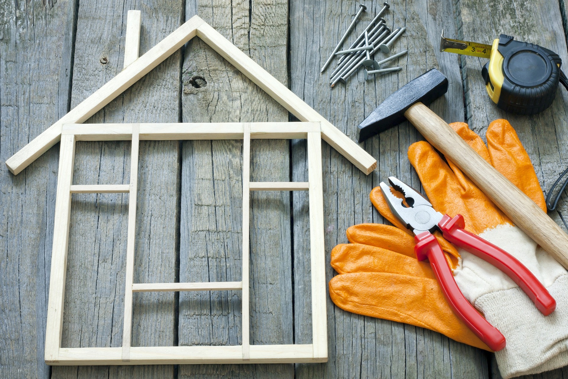 Kleines Holzhaus aus Stäben gebaut, Werkzeug daneben, Handschuhe, Hammer und Nägel